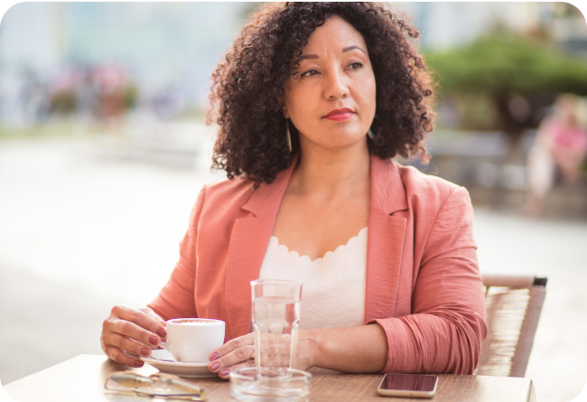 Woman in orange blazer enjoying coffee at a table alone